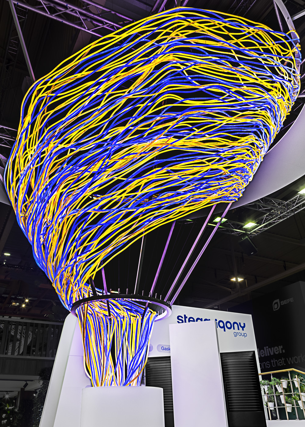 Detailansicht der ikonischen Lichtskulptur des Messestands der STEAG Iqony Group auf der E-world. Hunderte dynamisch verflochtener Lichtlinien verdichten sich zu einer schwebenden, organischen Form und visualisieren Energie, Vernetzung und Transformation – das zentrale Gestaltungselement des gesamten Messeauftritts.