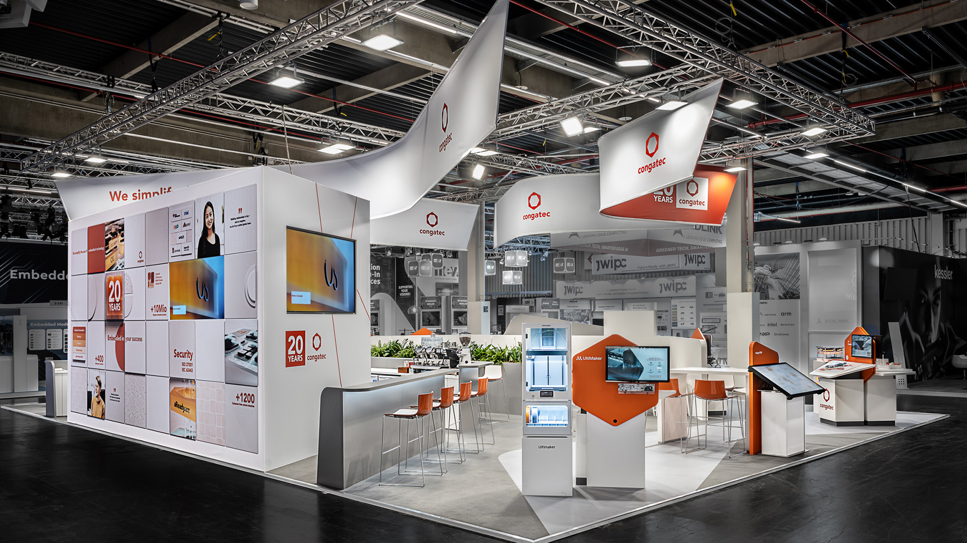 Messestand von Congatec auf der embedded world in Nürnberg mit 170 m² Ausstellungsfläche. Das Standkonzept greift die charakteristischen abgerundeten Formen der Congatec-Bildmarke auf und kombiniert sie mit der markanten CI-Farbe Orange. Organisch geschwungene Deckenbanner, wiederverwendbare Präsentationsmodule, interaktive Exponate und individuell entwickelte Produktpräsenter schaffen eine moderne Präsentationsfläche für Embedded-Computing-Technologien. Die klare Besucherführung, grafisch gestaltete Bodenflächen und hochwertige Detailausführungen sorgen für einen nachhaltigen, aufmerksamkeitsstarken Messeauftritt mit hoher Wiedererkennbarkeit.