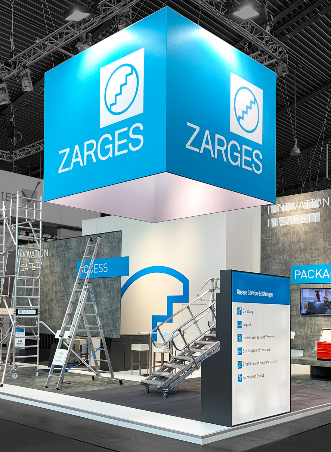 The central communication bar of the two-story SENS exhibition booth at Intersolar Smarter E in Munich features an organically shaped wooden counter, a striking LED ring light as an eye-catcher, open seating areas, green lounge zones, and transparent expanded metal architecture. The inviting booth concept combines design, sustainability, and communication across a 192 m² exhibition space.