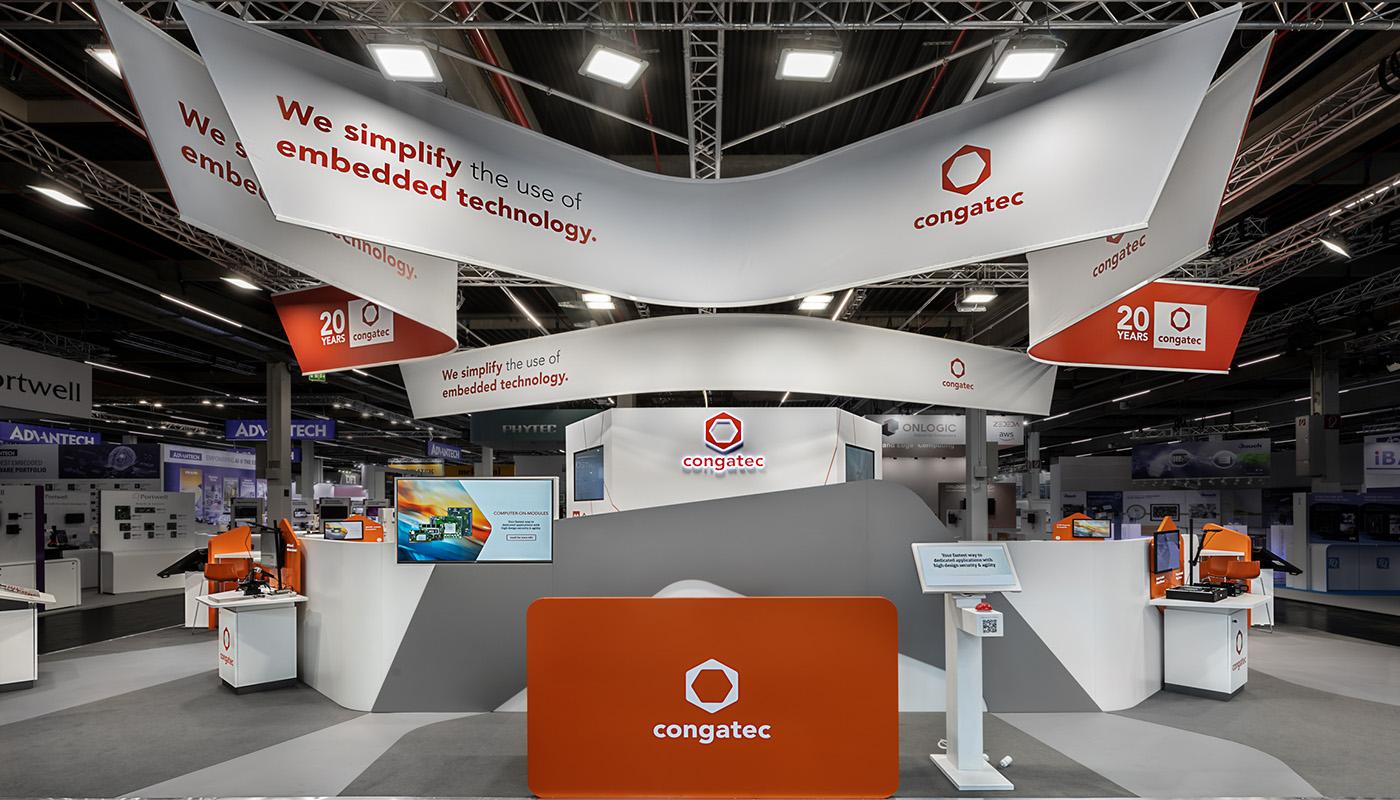 Congatec Messestand auf der embedded world Nürnberg: Moderner Technologiestand mit organisch geformten Deckensegeln, auffälliger CI in Orange und Weiß, modularen Produktpräsentern, interaktiven Demonstrationsflächen und wiederverwendbaren Messebauelementen für Embedded-Computerlösungen.