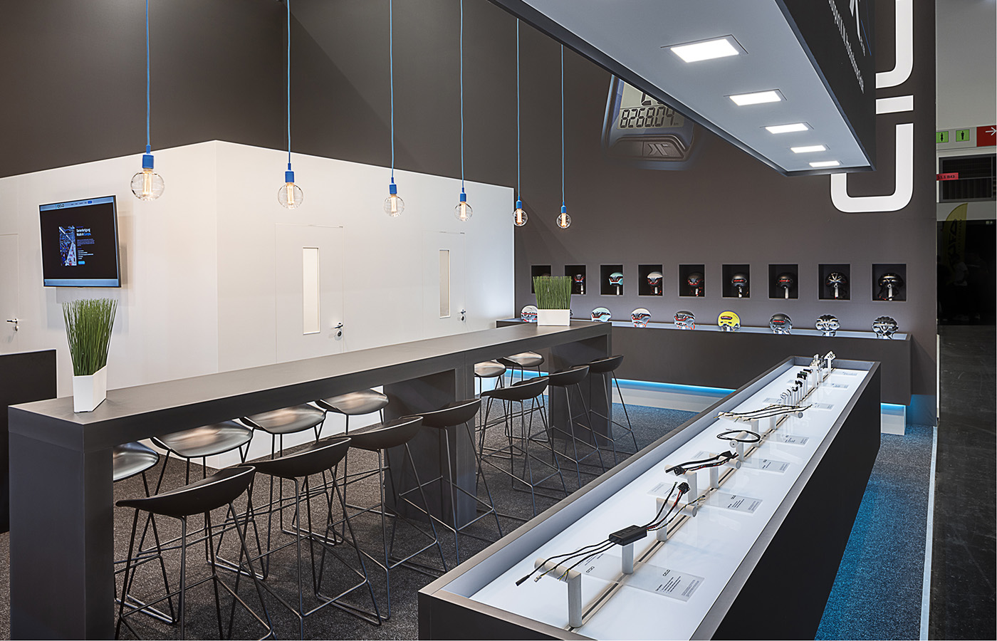 Detailansicht des Ciclo Sport Messestandes auf der Eurobike in Frankfurt mit beleuchtetem Produktpräsenter, hochwertigem Besprechungsbereich, minimalistischer Schwarz-Weiß-Architektur und blauen Lichtakzenten zur Präsentation von e-Bike-Komponenten.