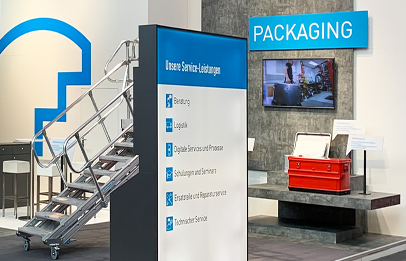 Detailaufnahme des ZARGES Messestands auf der LogiMAT in Stuttgart mit Präsentationsbereich für Packaging-Lösungen, Aluminium-Podesttreppe, Service-Stele, Produktdisplay und digitaler Medienwand.