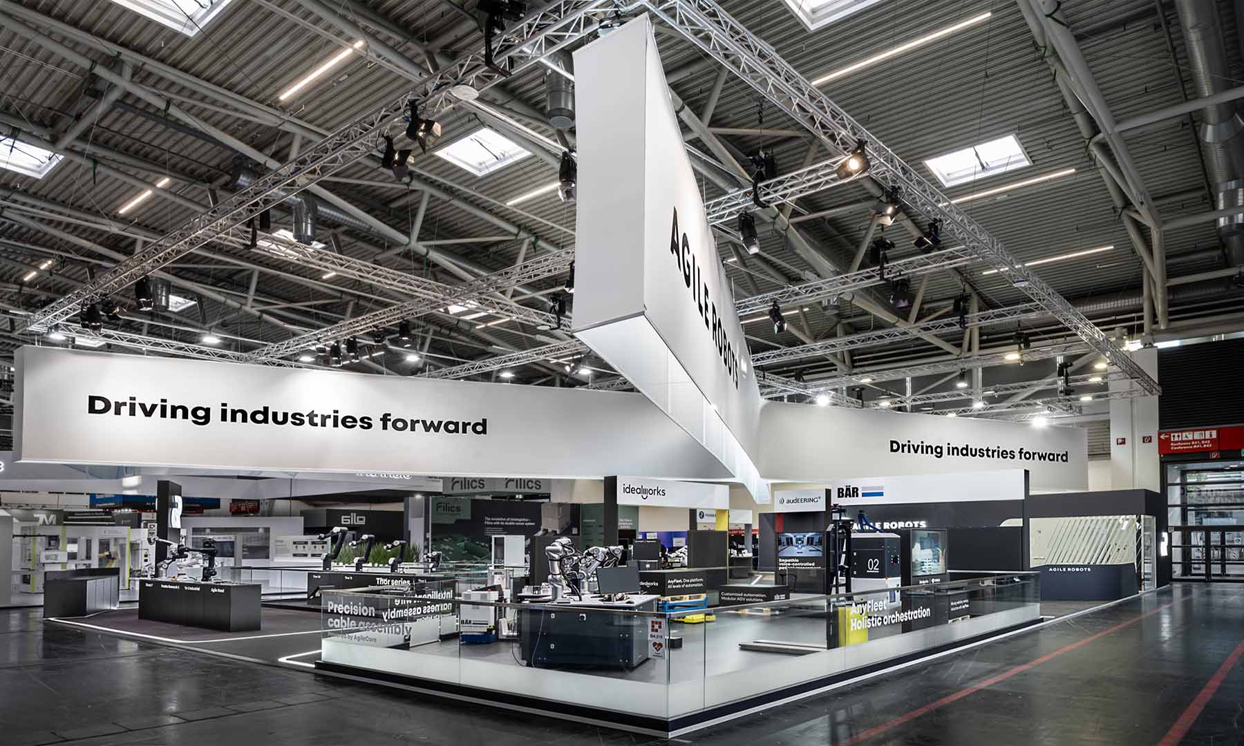 A panoramic view of Agile Robots’ 515 m² exhibition booth at automatica in Munich. The striking cross-shaped ceiling banner connects the presentation areas of the subsidiaries, while clean architecture, minimalist materials, and illuminated pathways create a modern stage for industrial robots and automation solutions throughout the entire exhibition space.