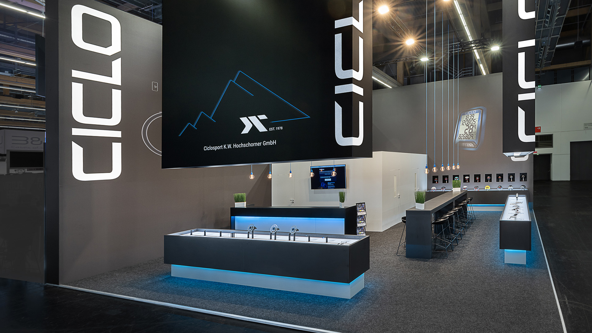 Messestand von Ciclo Sport auf der Eurobike in Frankfurt mit großformatigen, abgehängten Logoelementen, beleuchteten Produktpräsentern und minimalistischem Standdesign für hochwertige e-Bike-Komponenten.