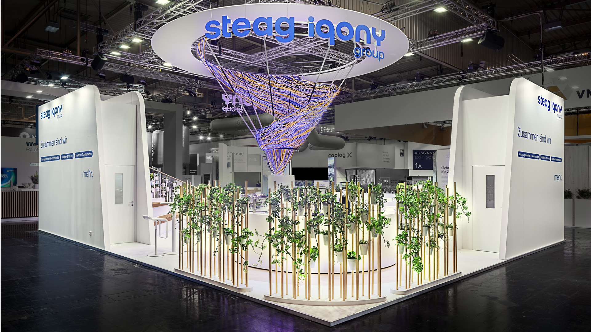 Messestand der STEAG Iqony Group auf der E-world mit einer skulpturalen Lichtinstallation als ikonischem Mittelpunkt. Die offene Standarchitektur, begrünte Gestaltungselemente und großzügige Kommunikationsbereiche verbinden Innovation, Nachhaltigkeit und persönliche Begegnung zu einem hochwertigen Markenerlebnis mit hoher Fernwirkung.