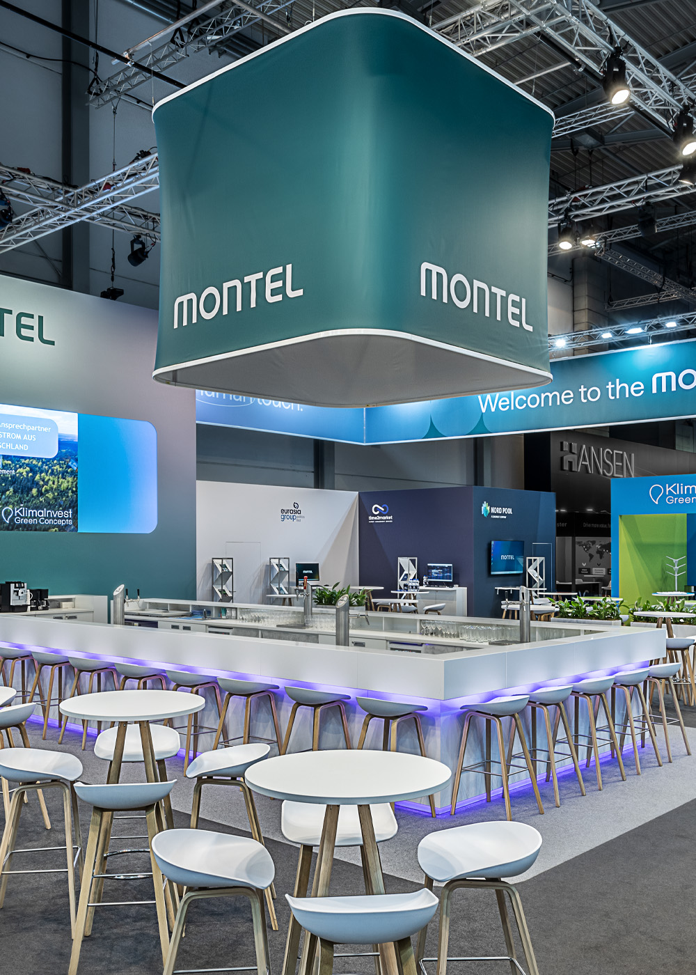 Moderner Messestand von Montel auf der E-world Energy & Water in Essen mit zentraler Bar, großem abgehängtem Deckenbanner, offenen Kommunikationsbereichen und nachhaltigem Standdesign für die Energiewirtschaft.