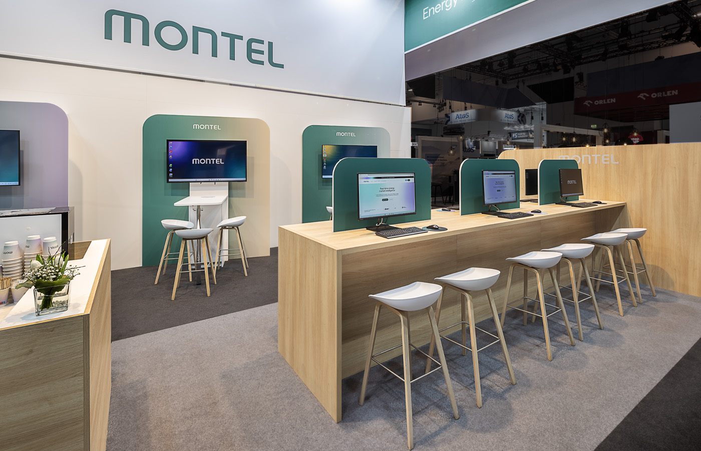 Arbeits- und Präsentationsbereich des Montel Messestands auf der E-world Energy & Water in Essen mit modernen Demo-Arbeitsplätzen, digitalen Informationsstationen und hochwertigem Holzdesign für den direkten Austausch mit Kunden.