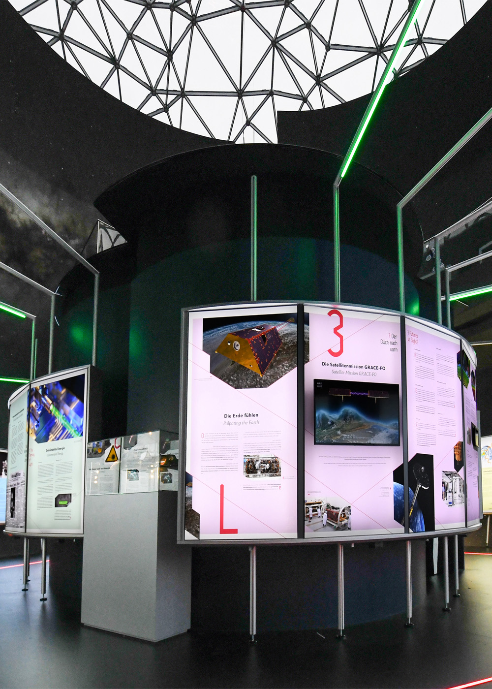 Zentrale Ausstellungsstation der interaktiven Ausstellung „Laser Licht Leben“ im ESO Planetarium Garching mit beleuchteten Informationstafeln, Multimedia-Inhalten und innovativer Präsentation moderner Lasertechnologie.