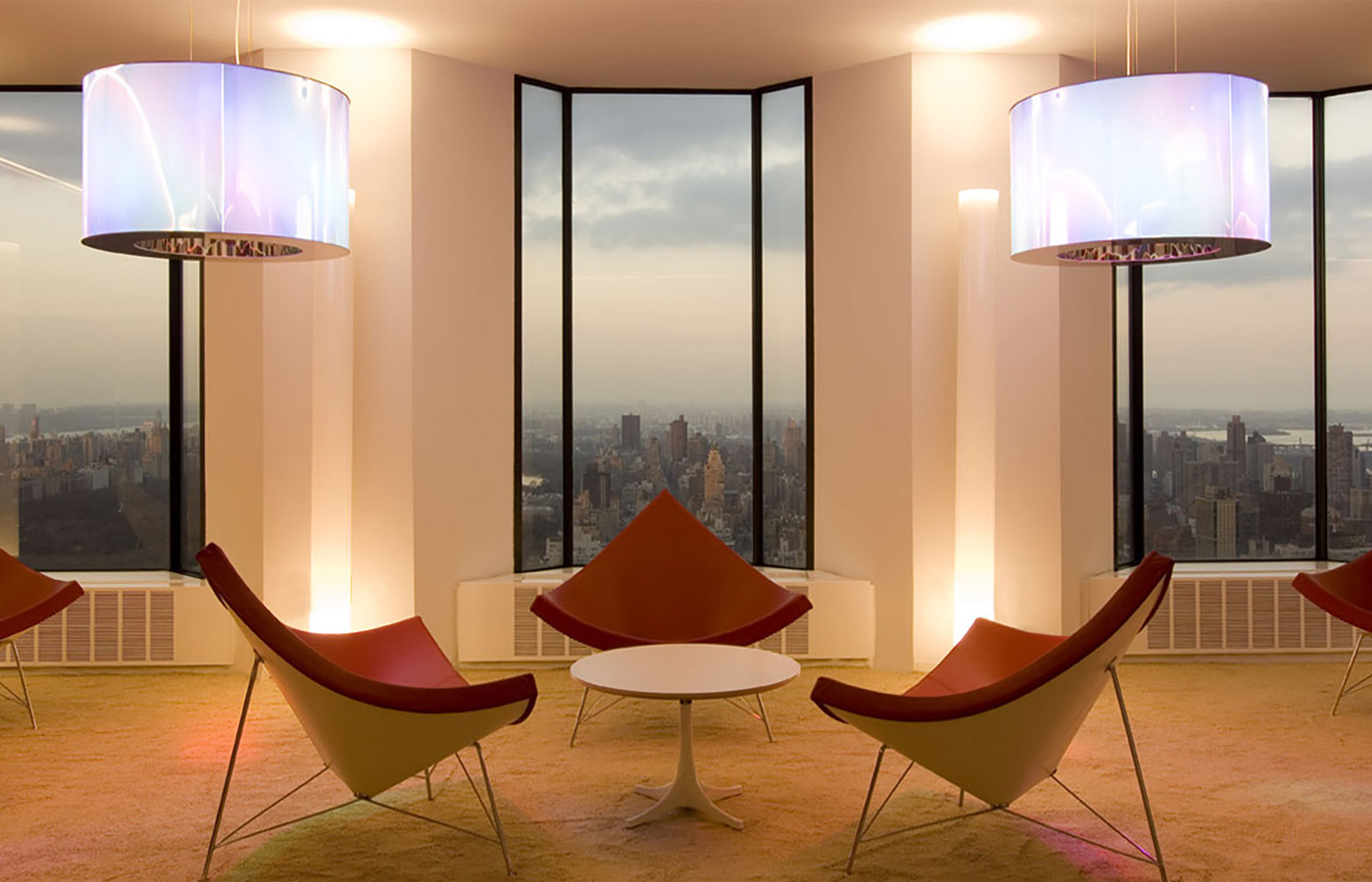 Design-Lounge mit ikonischen Sesseln, großzügigen Panoramafenstern und Blick auf die Skyline von Manhattan in einer modernen Büroetage in New York.