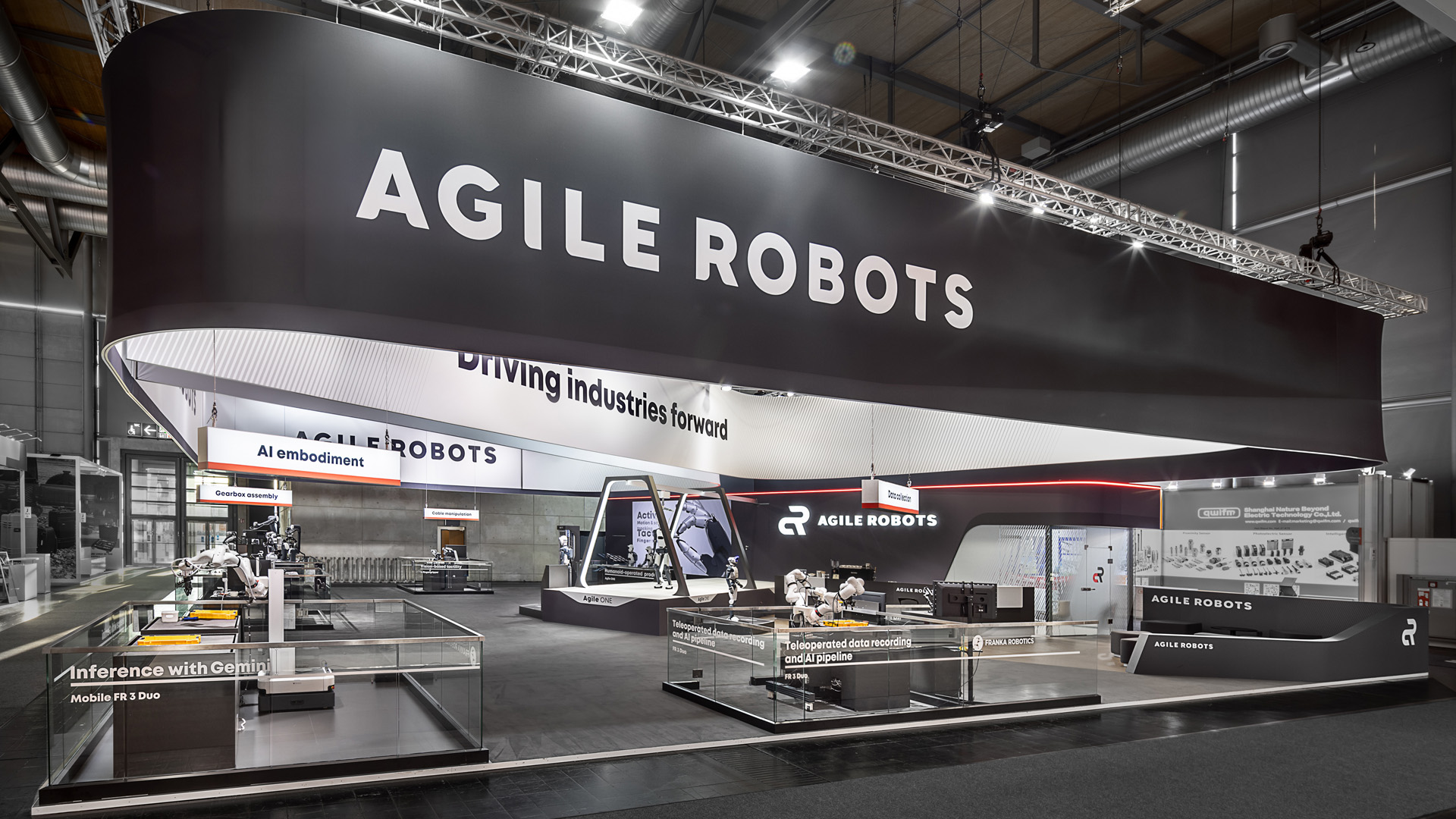 Messestand von Agile Robots auf der Hannover Messe mit großem, umlaufendem Deckenbanner, offenen Demonstrationsflächen und Live-Anwendungen für Robotik und KI. Die moderne Standarchitektur mit klaren Sichtachsen, hochwertiger Lichtführung und reduziertem Design setzt innovative Automatisierungslösungen eindrucksvoll in Szene.