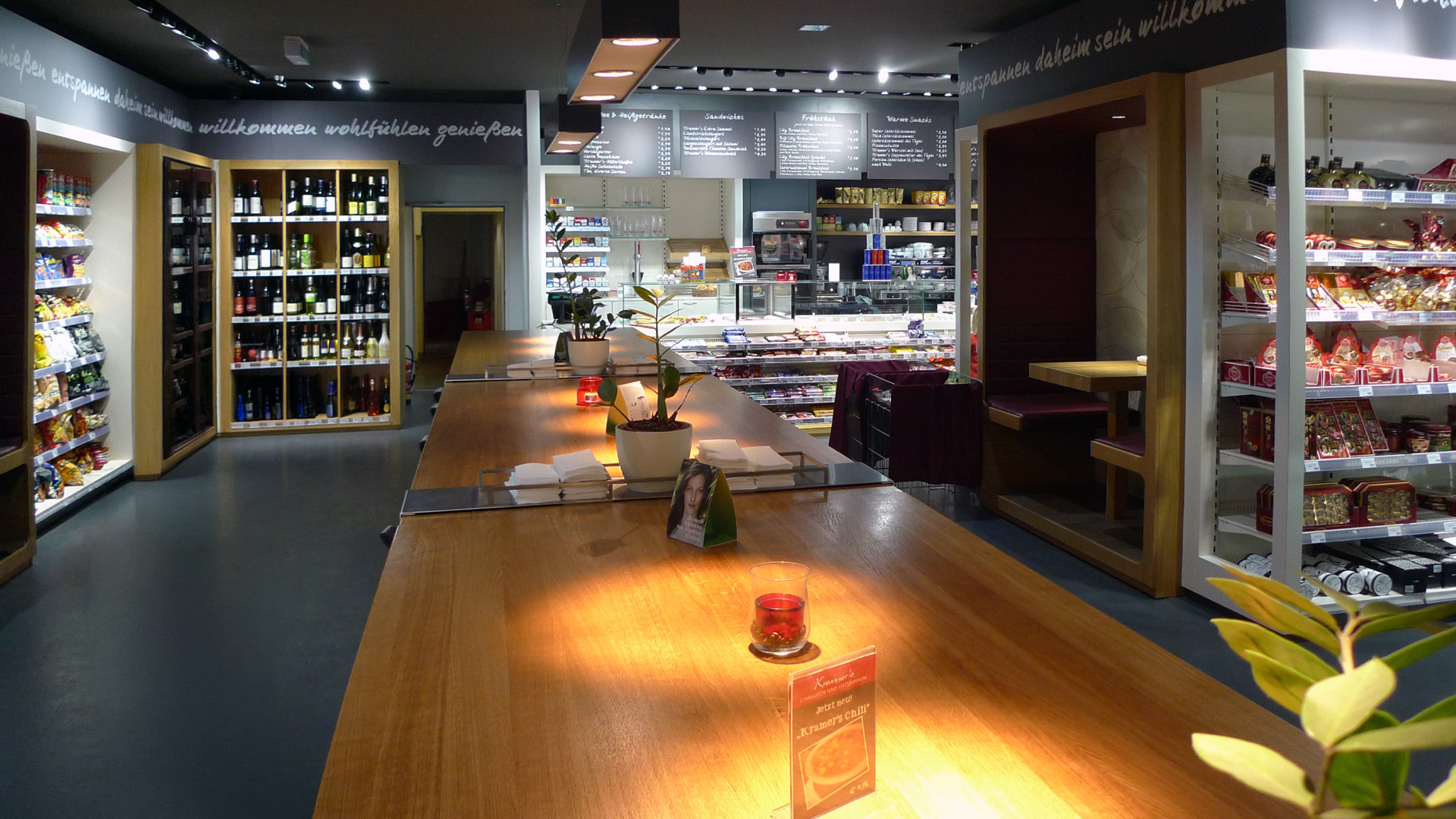 Zentraler Gemeinschaftstisch im Kramer's Café- und Convenience Store in Salzburg und Innsbruck mit integrierten Sitznischen, Weinregal und Gastronomiebereich.