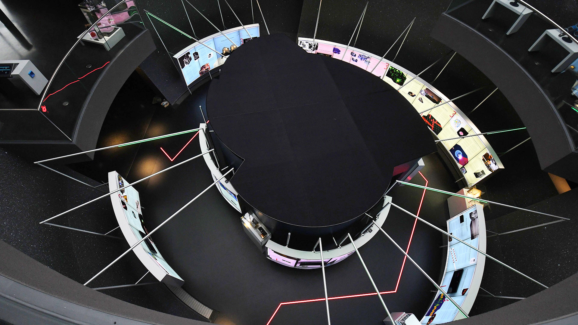 Draufsicht der Ausstellung „Laser Licht Leben“ im ESO Planetarium Garching mit radial angeordneten Informationsstationen, interaktiven Exponaten und zentralem Ausstellungsbereich zur Vermittlung moderner Lasertechnologie und Photonik.