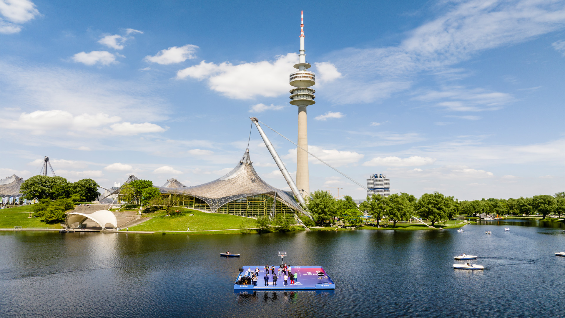 A floating basketball court on the Olympic Lake in Munich’s Olympic Park—an event project by Rapid Peaks for FC Bayern Basketball and BMW, featuring spectacular event architecture against the backdrop of the Olympic Tower.