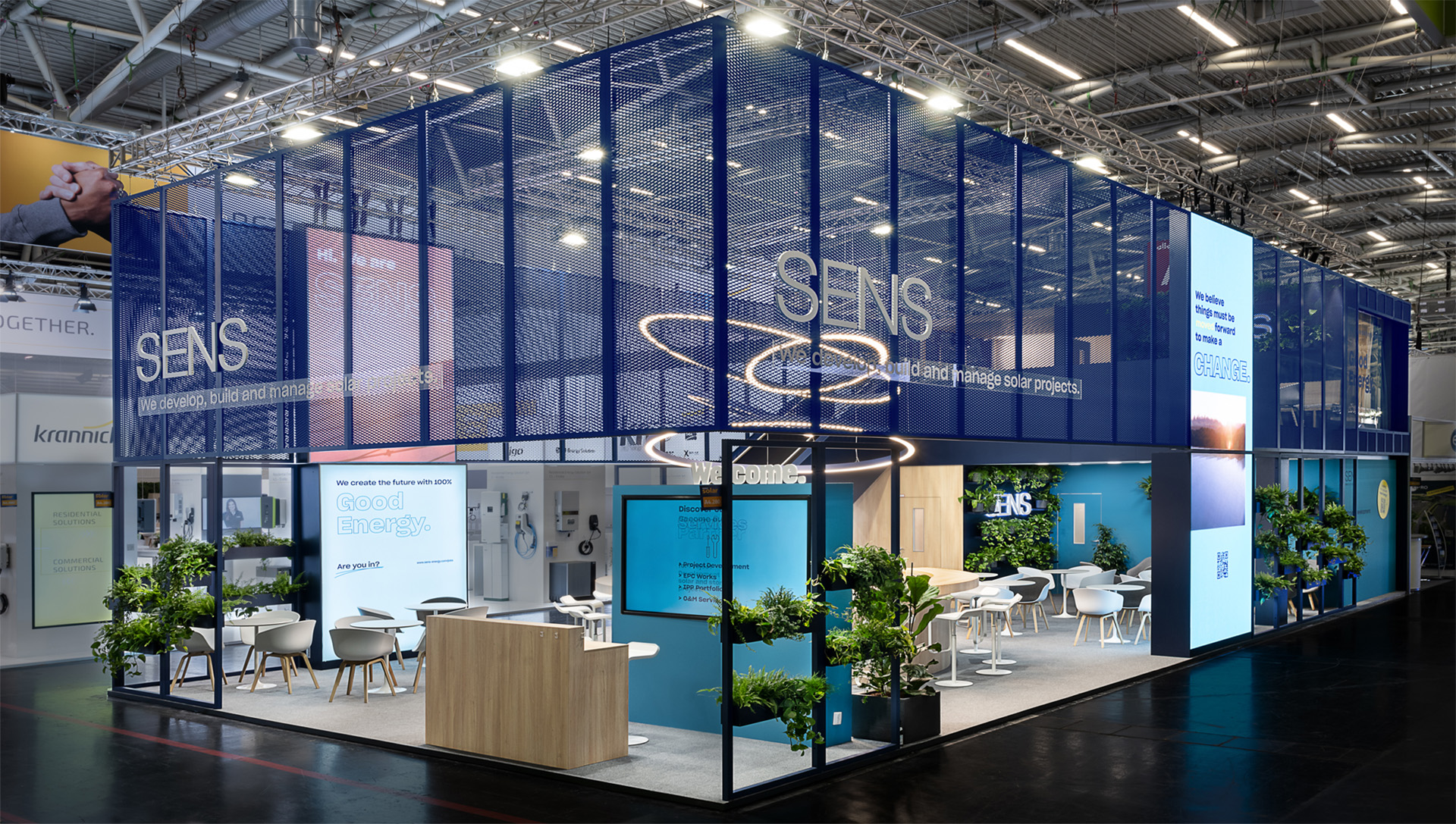 Großzügiger Doppelstock-Messestand von SENS auf der Intersolar Smarter E in München mit markantem, abgehängtem Streckmetall-Rahmen, zahlreichen Pflanzen, offenen Kommunikationsbereichen, runder Bar mit Lichtinstallation sowie modernen Meetingräumen für Beratung und Austausch in nachhaltiger Atmosphäre.