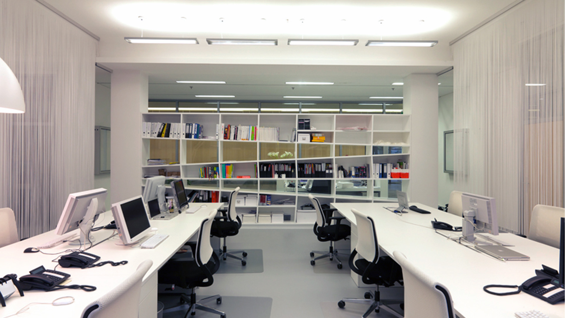 Offene Grafikabteilung einer Werbeagentur in München mit weißen Arbeitsplätzen, transparentem Regalsystem als Raumteiler und lichtdurchflutetem Open-Space-Büro.